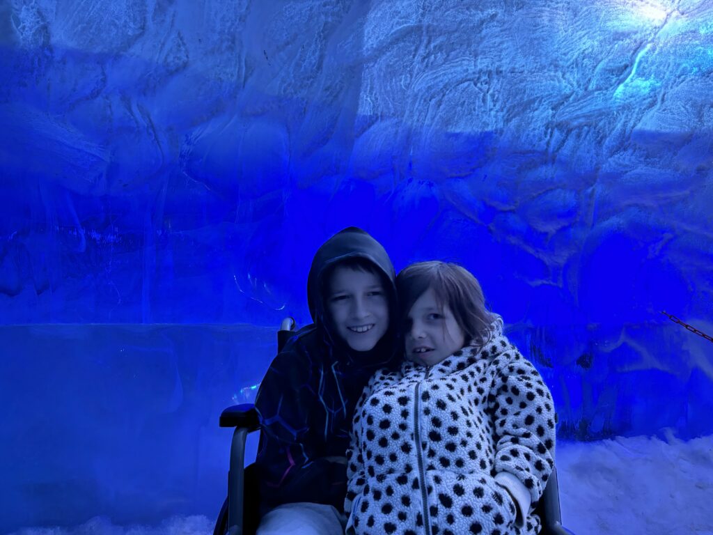 A young boy and girl huddled together smiling in a wheelchair in an ice cave.