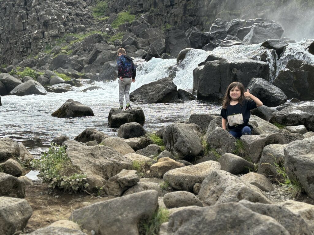 Max and Z at play at the base of a waterfall at thingvellir. Z is giving a grinning thumbs-up to the camera